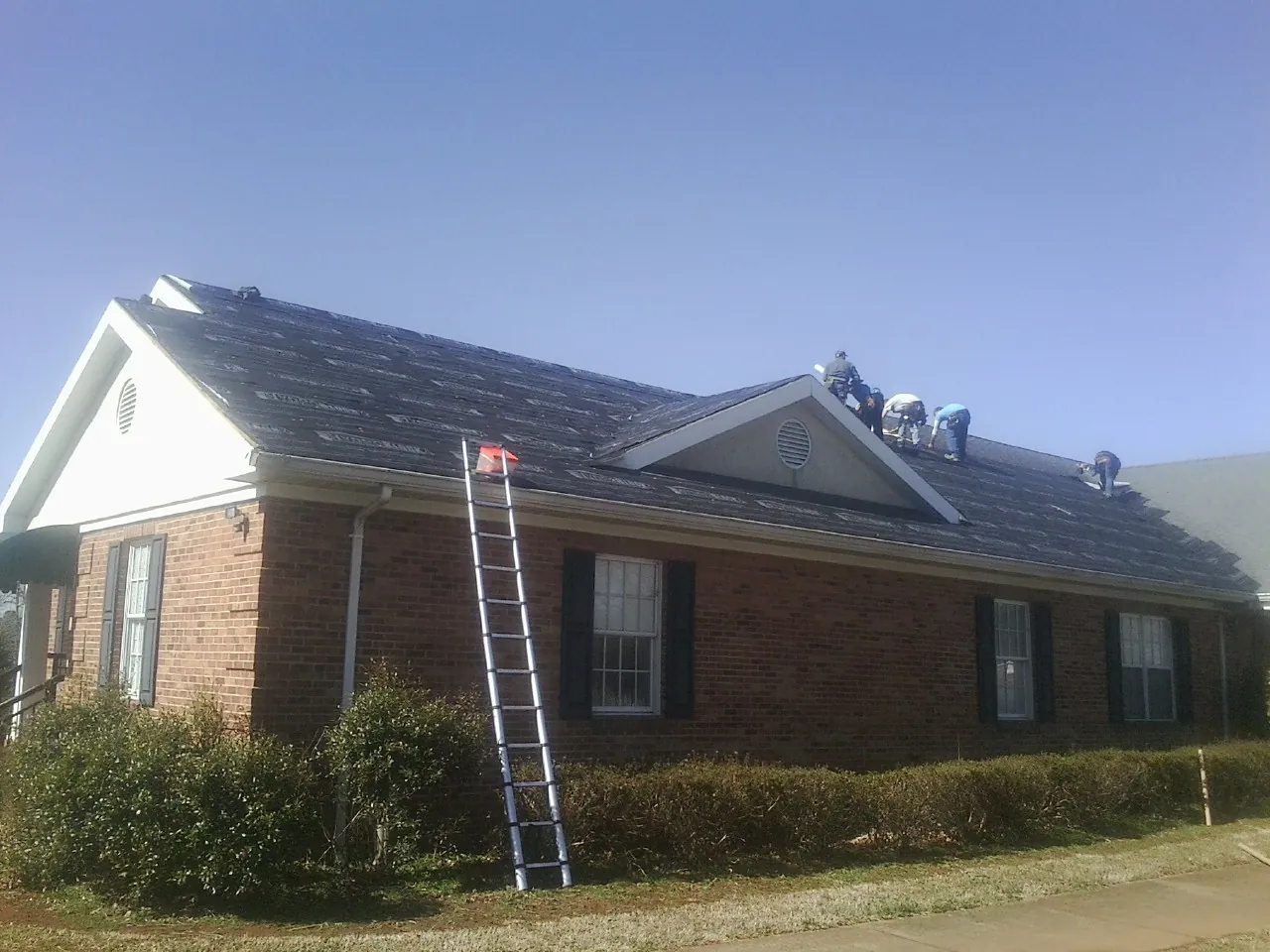 Crew tearing shingles off a brick ranch roof with a ladder set — Emergency Roof Repair work by our crew in Portland