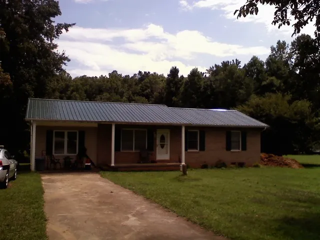 Dark green metal roof on a brick ranch with a covered porch in Portland